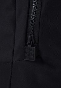 Détail de fermeture éclair en tissu noir avec une tirette texturée en forme carrée et un motif en grille, intégrée dans un matériau robuste.