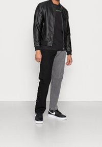Chaqueta bomber de piel negra, jeans desgastados en negro y gris, y zapatillas negras con acentos en blanco. Camiseta básica de cuello redondo debajo.
