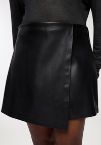 Mini gonna in pelle nera con design avvolgente, caratterizzata da una texture liscia e un orlo leggermente svasato, che offre una silhouette aderente.