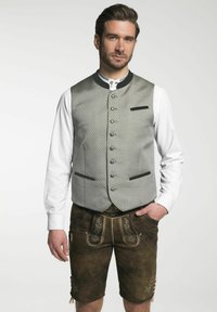 Šedá vzorovaná vesta s černými akcenty, zapínání na knoflíky, spárovaná s hnědými lederhosen, které mají vyšívané detaily a kapsy.