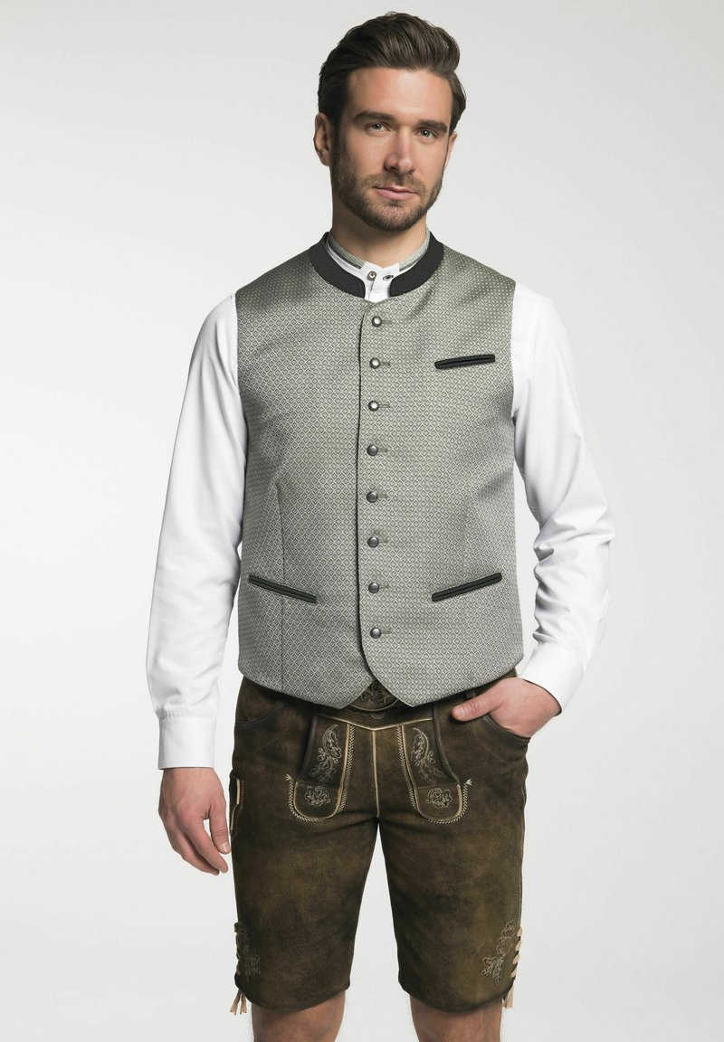 Grau gemusterte Weste mit schwarzen Akzenten, durchgehende Knopfleiste, kombiniert mit braunen Lederhosen mit bestickten Details und Taschen.