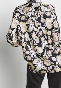 Camicia nera a fiori con vestibilità oversize, caratterizzata da motivi di fiori rosa e gialli, colletto e maniche arrotolate. Tessuto morbido.