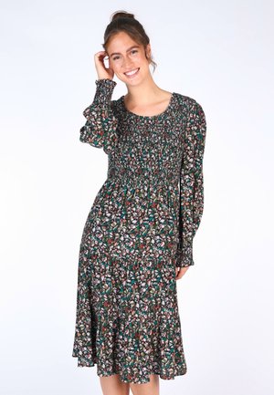 Blumenkleid mit rüschiertem Oberteil, langen puffärmel und ausgestelltem Rock. Die Farben umfassen Grün, Braun und Weiß, mit einem strukturierten Stoff.