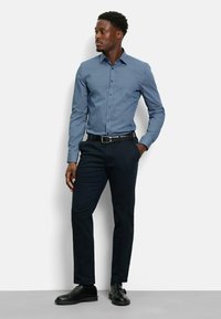 Hemd mit Knöpfen in Marineblau mit einem kleinen weißen geometrischen Muster, kombiniert mit dunklen Hosen und schwarzen Schuhen. Slim-Fit-Design mit langen Ärmeln.