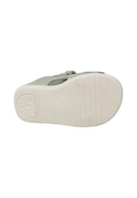 Scarpa grigia chiara con tomaia liscia, cinturino regolabile e suola in gomma bianca texturizzata con scanalature per una maggiore aderenza.