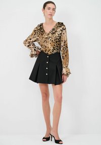 Blusa con stampa leopardata e scollatura arricciata, abbinata a una gonna nera plissettata con bottoni in tonalità oro. Tacchi aperti neri completano il look.