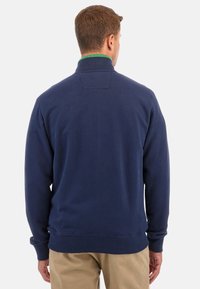 Mörkblå sweatshirt med hög krage, ribbade muddar och fåll. Har en subtil struktur och en accent i grönt vid kragen.