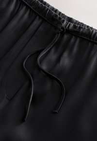 Ceinture élastique en tissu noir avec cordon de serrage à deux fils lâches et coutures visibles sur un matériau doux à la texture lisse.