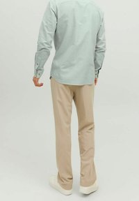 Lichtgroene long-sleeve shirt met knoopmanchetten, gecombineerd met beige broek en witte sneakers. Het shirt heeft een gebogen zoom en een relaxte pasvorm.