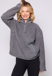 Pullover grigio in pile con colletto a mezza zip, tessuto testurizzato e tasche laterali con dettagli a contrasto. Vestibilità comoda e maniche lunghe.