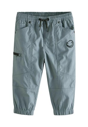Pantalon court bleu clair avec taille et poignets élastiques, poches avant, une poche zippée latérale et un petit motif smiley circulaire sur le côté droit.