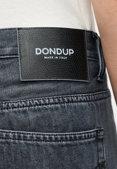 Gros plan sur un jean en denim noir avec une étiquette en cuir texturé noir portant l'inscription "DONDUP Made in Italy" sur la ceinture.