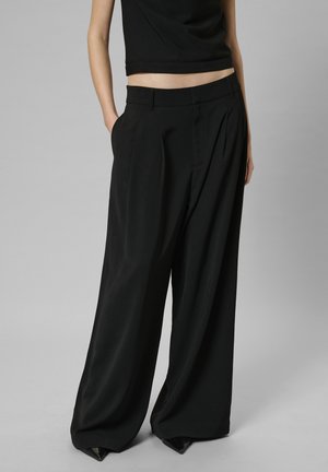 Czarne szerokie spodnie z gładkiego materiału, z głębokimi zakładkami, bocznymi kieszeniami i talią z przeznaczeniem do szycia. Połączone z krótkim topem.