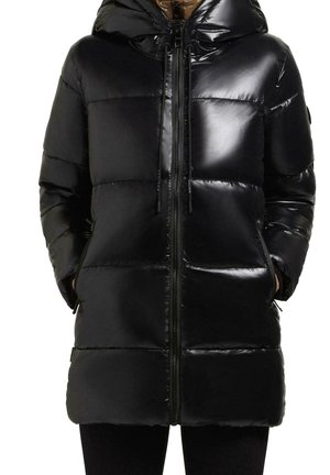 Manteau matelassé noir brillant avec capuche, fermeture éclair devant, poches latérales et un design matelassé, porté les mains dans les poches.