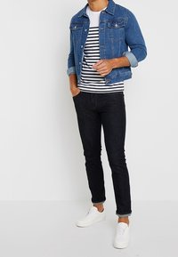 Chaqueta de denim azul con detalles de botones, camiseta de rayas blanca y azul marino, jeans negros ajustados y zapatillas blancas. Un atuendo simple y casual.