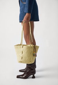 Geflochtene Strohtasche mit zwei strukturierten, gedrehten Griffen und bunten Perlenakzenten, mit einem runden Boden und offenem Topdesign.