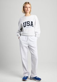 Set di felpa grigia e pantaloni tuta, con una grafica "USA" nera. Tessuto morbido, vestibilità comoda, con cintura elastica e tasche. Sneakers blu.