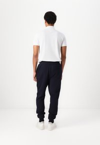 Camisa polo blanca y pantalones de chándal azul marino con puños elásticos, con una textura suave y un detalle de bolsillo en la parte posterior.