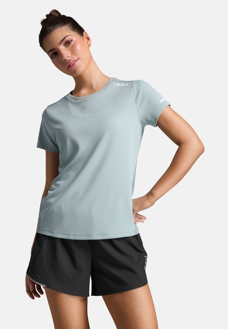 Světle modré sportovní tričko vyrobené z hladkého materiálu, s krátkým rukávem, kulatým výstřihem a logem na rameni; v kombinaci s černými šortkami.
