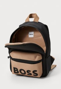 Črna in rjava nahrbtnik, narejen iz trpežne tkanine, z glavno zadrgo, sprednjim žepom na zadrgo in oznako z logotipom "BOSS".