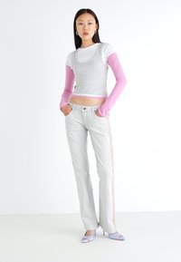 Top corto gris sobre una camiseta de manga larga blanca, jeans gris claro con raya lateral y tacones destalonados azules. Texturas suaves y diseño ajustado.