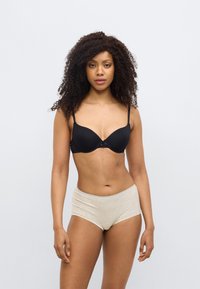 Μαύρο επενδυμένο σουτιέν με ρυθμιζόμενους ιμάντες και διακοσμητικό φιόγκο στο κέντρο, συνδυασμένο με ανοιχτό μπεζ ψηλόμεσο σλιπ. Λείο, απαλό υλικό.