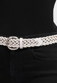 Hvid flettet læderbælte med spænde i sølvtonet dobbelt ring, der har en glat tekstur og et elegant design, båret over sorte bukser.