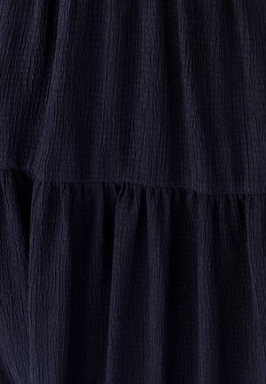 Tumši zils kropls audums ar teksturētu virsmu, kas veidots ar kārtainu dizainu un savāktām šuvēm, radot mīkstu un vieglu izskatu.