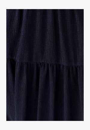 Tumši zils kropls audums ar teksturētu virsmu, kas veidots ar kārtainu dizainu un savāktām šuvēm, radot mīkstu un vieglu izskatu.