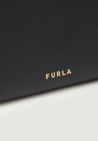Piele texturată neagră cu un logo "FURLA" auriu în contrast. Vedere de aproape care subliniază detalii privind materialul și brandul.