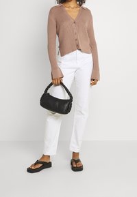 Tan geribbelde gebreide cardigan met lange mouwen en knopen, gecombineerd met witte rechte jeans en een zwarte gevlochten handtas. Zwarte platform slippers.