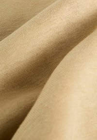 Gros plan sur un tissu beige avec une texture fine en maille et des plis doux créant des ombres délicates.