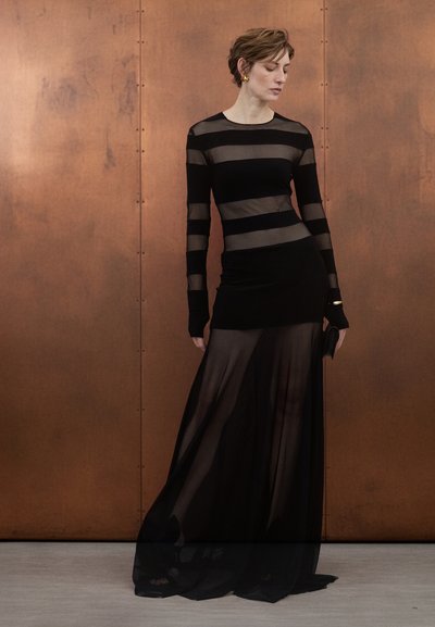 Črna prosojna obleka z dolgimi rokavi z vodoravnimi črtami. Prilegajoč se korzet se preliva v puhasto krilo. Preprost okrasni ročaj.