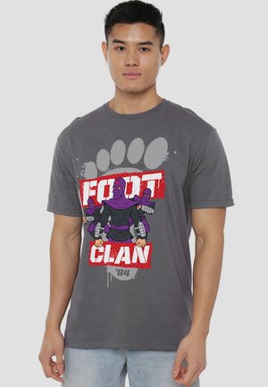 Graues Baumwoll-T-Shirt mit einem grafischen Design von drei lila Charakteren und dem Text "FOOT CLAN" in Weiß und roten Akzenten.