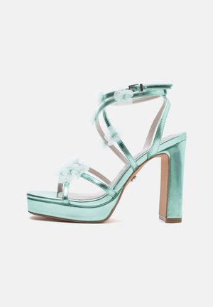 Sandalo con tacco alto verde menta metallico con suola piattaforma, cinturino alla caviglia con fibbia e decorazioni floreali bianche sui cinturini.