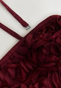 Burgundia kangastop, millel on lillede aplikatsioon kihilisest ja tekstureeritud õitest; reguleeritavad rihmad ja hõbedased detailid.