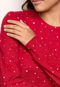 Czerwony longsleeve z miękkiego materiału, ozdobiony białym wzorem gwiazd, z okrągłym dekoltem i dopasowanymi rękawami.