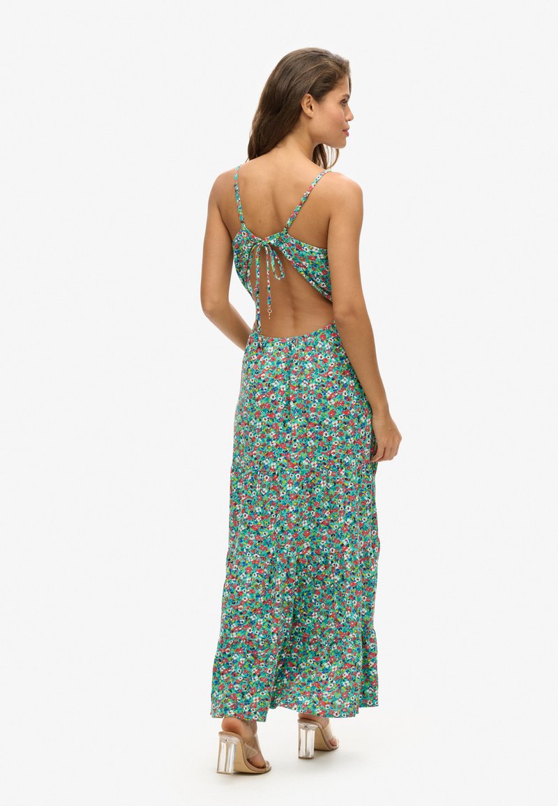 Kwiatowa maxi sukienka w kolorze zielonym z czerwonymi i białymi wzorami. Posiada cienkie, regulowane ramiączka oraz otwarty tył z detalem nawiązywanym wstążką. Zwiewna spódnica.