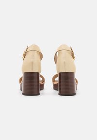 Goldene Leder-Sandalen mit einem Holzblockabsatz. Offenes Zehendesign, Knöchellasche mit goldener Schnalle und strukturierter Oberflächenbeschaffenheit.