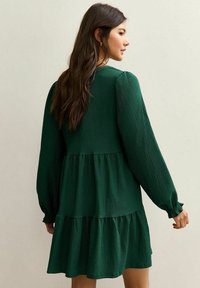 Zielona, teksturowana sukienka z długimi, bufkami rękawami, warstwową spódnicą i elastycznymi mankietami. Materiał ma subtelny, żeberkowy wzór.