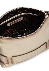 Indvendig i en metallic beige lædertaske med lynlås, prydet med et mønstret stoffor og et mærketikette. Teksturerede materialer synlige.