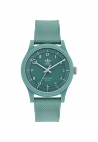 Montre solaire verte avec un bracelet en caoutchouc texturé. Cadran rond avec des marqueurs d'heure blancs et des marquages de minutes noirs, arborant un logo Adidas.