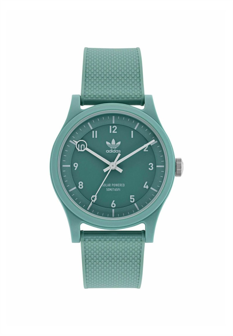 Montre solaire verte avec un bracelet en caoutchouc texturé. Cadran rond avec des marqueurs d'heure blancs et des marquages de minutes noirs, arborant un logo Adidas.