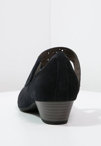 Chaussure en daim noir avec un dos fermé, des accents découpés et un talon bas texturé. Surface lisse avec un design à bout rond.