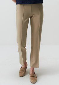 Pantaloni beige su misura con una texture liscia, frontale piatto e sottili spacchi laterali all'orlo, abbinati a scarpe slip-on beige chiaro.