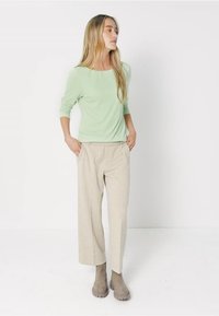 Hellgrünes Langarmoberteil kombiniert mit beigen weitem Hosen und grauen Knöchelstiefeln, die ein einfaches Design und eine entspannte Passform aufweisen.