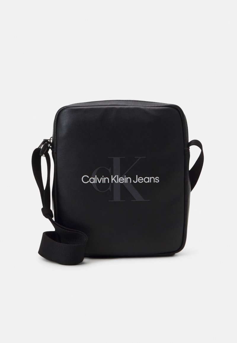 Borsa crossbody nera in materiale sintetico morbido, con il logo "Calvin Klein Jeans" in bianco. Include una tracolla regolabile.