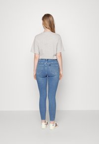 Camisa de algodón gris de manga corta, combinada con pantalones vaqueros ajustados de color azul claro y zapatillas blancas con rayas burdeos, vista desde la parte de atrás.