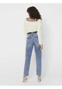 Blusa amarilla claro de manga larga con escote cuadrado, combinada con jeans de tiro alto azul claro. Accesorios con un cinturón negro y zapatos de tacón blancos.