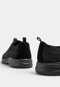 Svarta atletiska skor med en texturerad stickad ovandel, mockadetaljer och en flexibel svart sula. Dragflik bak för enkel påtagning.